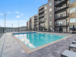 A swimming pool with a clear blue water, surrounded by lounge chairs and a building with balconies. - Black Rock 418 | 2BR Mountain Retreat with Pool & Hot Tub (Heber City)