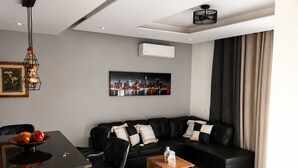 A modern living room with a black leather sofa, a wooden coffee table, a dining area with a black table and chairs, and a cityscape painting on the wall. - Apartment Achada St Antonio Rua Principal AC, WIFI (Praia)