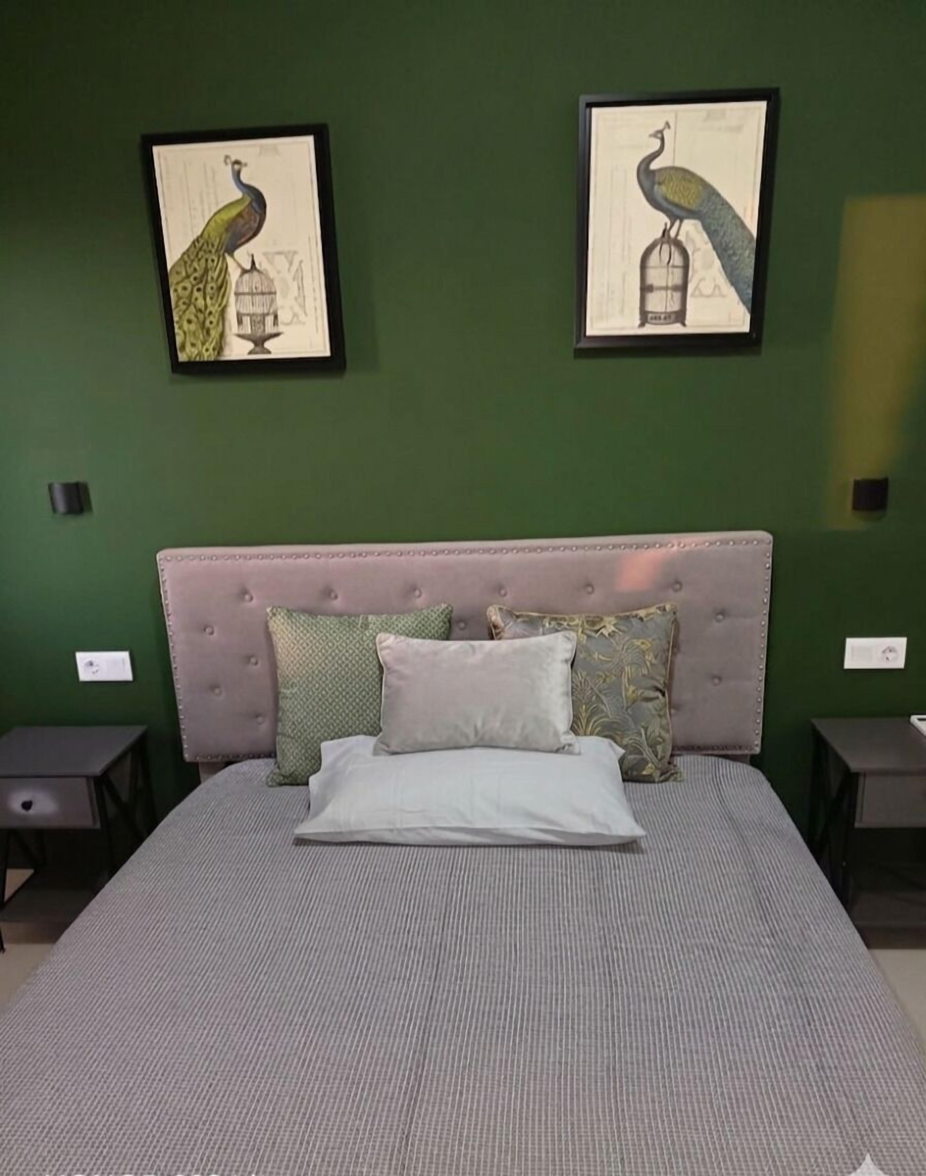 Ein Schlafzimmer mit grüner Wand, einem gepolsterten Kopfteil, einem Bett mit gestreifter Bettdecke und zwei gerahmten Kunstwerken mit Vogelmotiven.