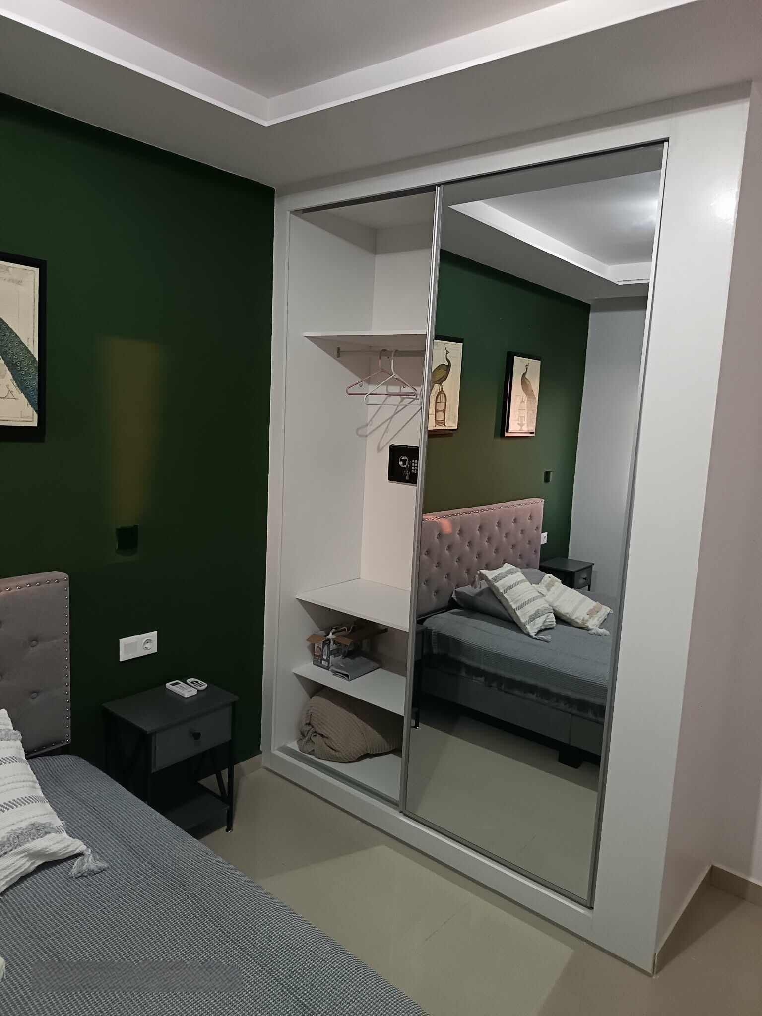 A bedroom with a bed, a nightstand, a wardrobe, and a mirror.