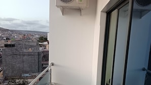 A balcony with a white air conditioning unit, a glass door, and a city view. - Apartment Achada St Antonio Rua Principal AC, WIFI (Praia)