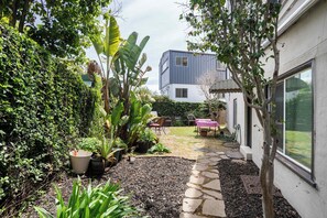 Ein Garten mit einem Kiesweg, Kübelpflanzen und einer Terrasse mit Gartenmöbeln.