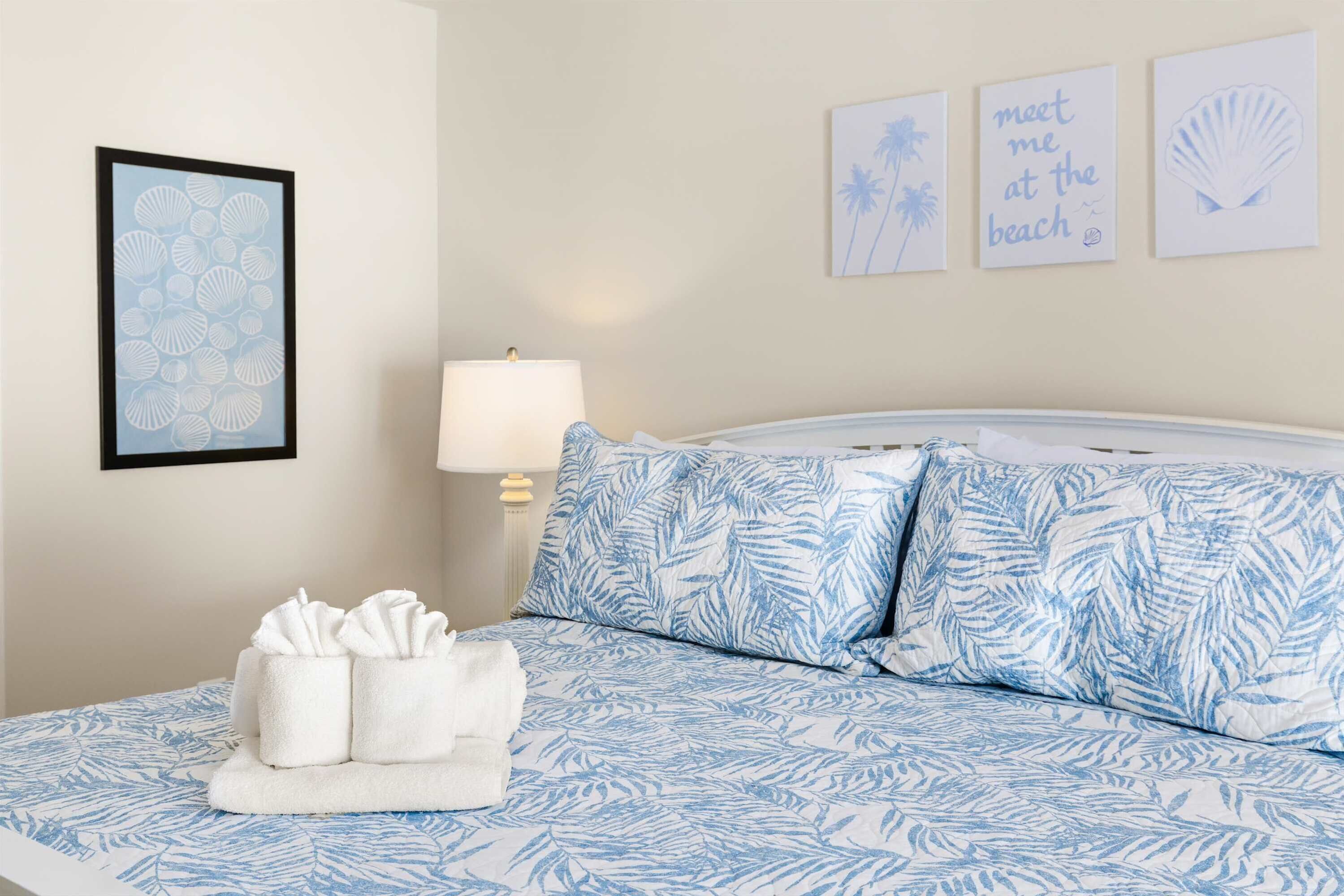 A bedroom with a bed, pillows, a bedside table, a lamp, and wall art.