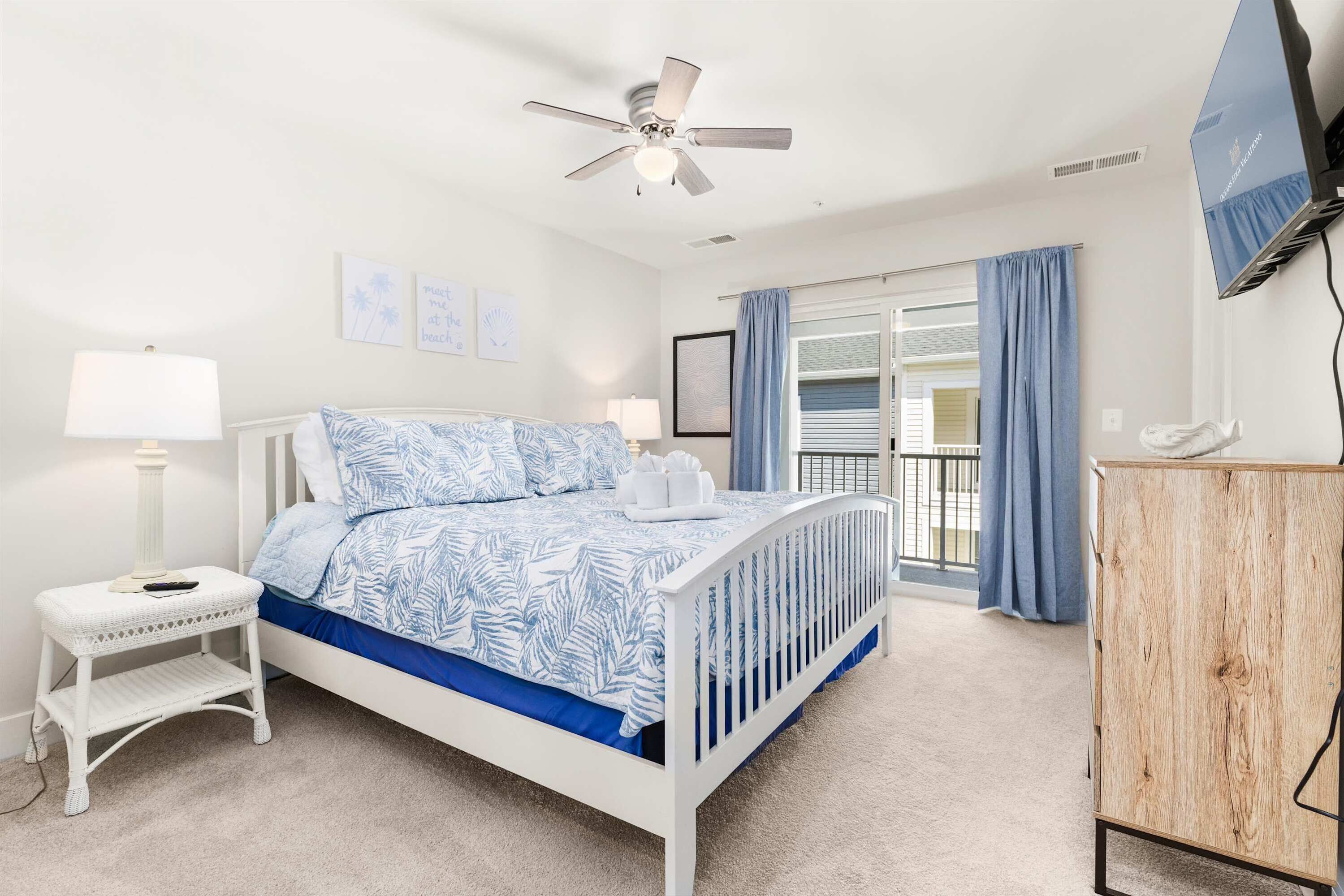 A bedroom with a bed, a nightstand, a wooden cabinet, a ceiling fan, and a window with curtains.