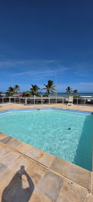 Una piscina azul cristalina con borde de azulejos, rodeada de palmeras y vistas al océano.