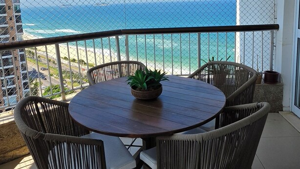 Una mesa redonda con sillas de mimbre y una planta en maceta en un balcón con vistas al océano.