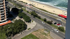 Vista costera con playa, océano y una carretera que lleva a un edificio de varios pisos.