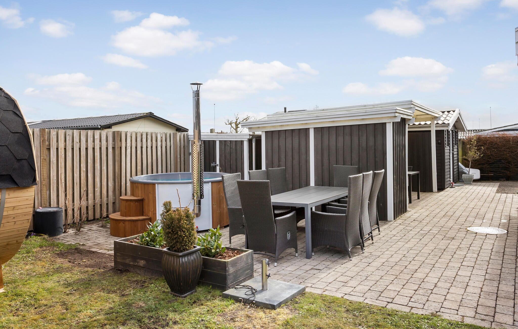 Un jardin avec un jacuzzi, du mobilier de jardin et une zone délimitée par une clôture.