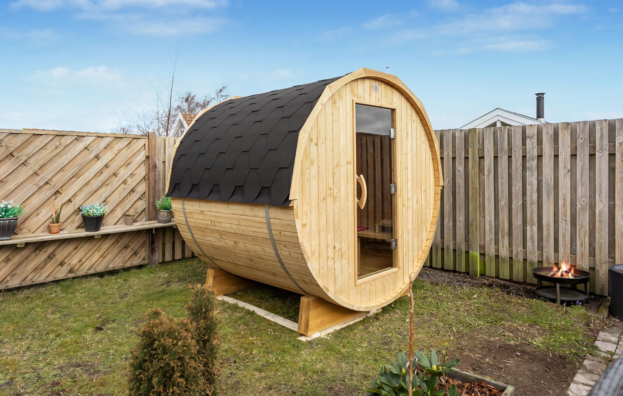 Una sauna de madera con techo inclinado, puerta de cristal y una chimenea en el patio trasero.