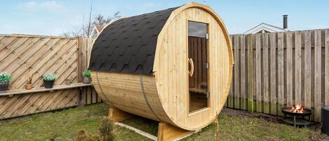 Una sauna de madera con techo inclinado, puerta de cristal y una chimenea en el patio trasero.