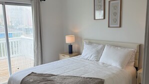 Et soveværelse med en seng, et natbord, en lampe, en ventilator i loftet og billeder i rammer på væggen.