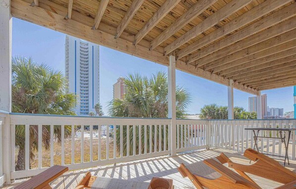 Un espace extérieur abrité, aménagé avec du mobilier en bois et offrant une vue sur de hauts immeubles et des palmiers.