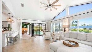 A spacious living area with a large sofa, a dining table, and a view of a pool. - Gulfstream Getaway | Vesteva Rentals | Gulf Access Canal | Coastal Flair (Cape Coral)