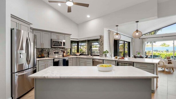 A modern kitchen with a large island, stainless steel appliances, and a view of the outdoors. - Gulfstream Getaway | Vesteva Rentals | Gulf Access Canal | Coastal Flair (Cape Coral)