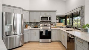 A modern kitchen with stainless steel appliances, grey cabinetry, and a wooden floor. - Gulfstream Getaway | Vesteva Rentals | Gulf Access Canal | Coastal Flair (Cape Coral)