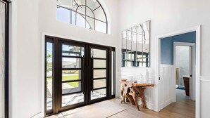 A spacious room with a large sliding glass door leading to a patio, a wooden coffee table, and a large mirror on the wall. - Gulfstream Getaway | Vesteva Rentals | Gulf Access Canal | Coastal Flair (Cape Coral)