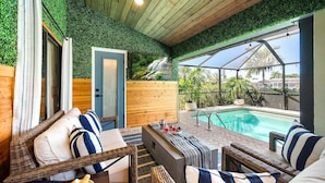 A covered outdoor seating area with wicker furniture, a pool, and a view of a waterfall. - Gulfstream Getaway | Vesteva Rentals | Gulf Access Canal | Coastal Flair (Cape Coral)