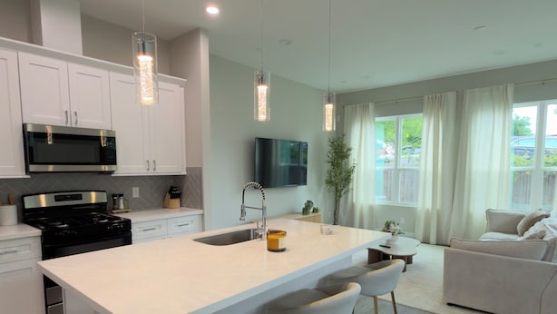 Uma cozinha moderna com armários brancos, uma ilha central com banquetas, micro-ondas embutido e iluminação pendente.