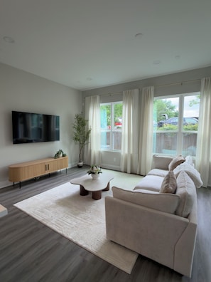 Ein modernes Wohnzimmer mit Sofa, Couchtisch, Fernseher und einer Zimmerpflanze.