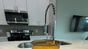 Cozinha com armários brancos, micro-ondas de aço inoxidável, pia e uma vela com a etiqueta 'SCENTSATIONAL Storm No. 06'.