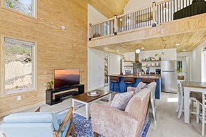 A spacious living area with a large TV, comfortable seating, a kitchen with bar stools, and a wooden ceiling. - Modern Cabin Nestled in the Smoky Mountains (Sevierville)