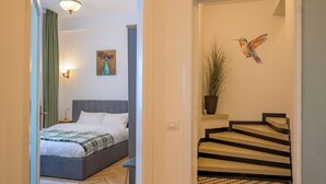 A bedroom with a bed, a nightstand, a wall-mounted light, a painting, and a staircase with a potted plant.