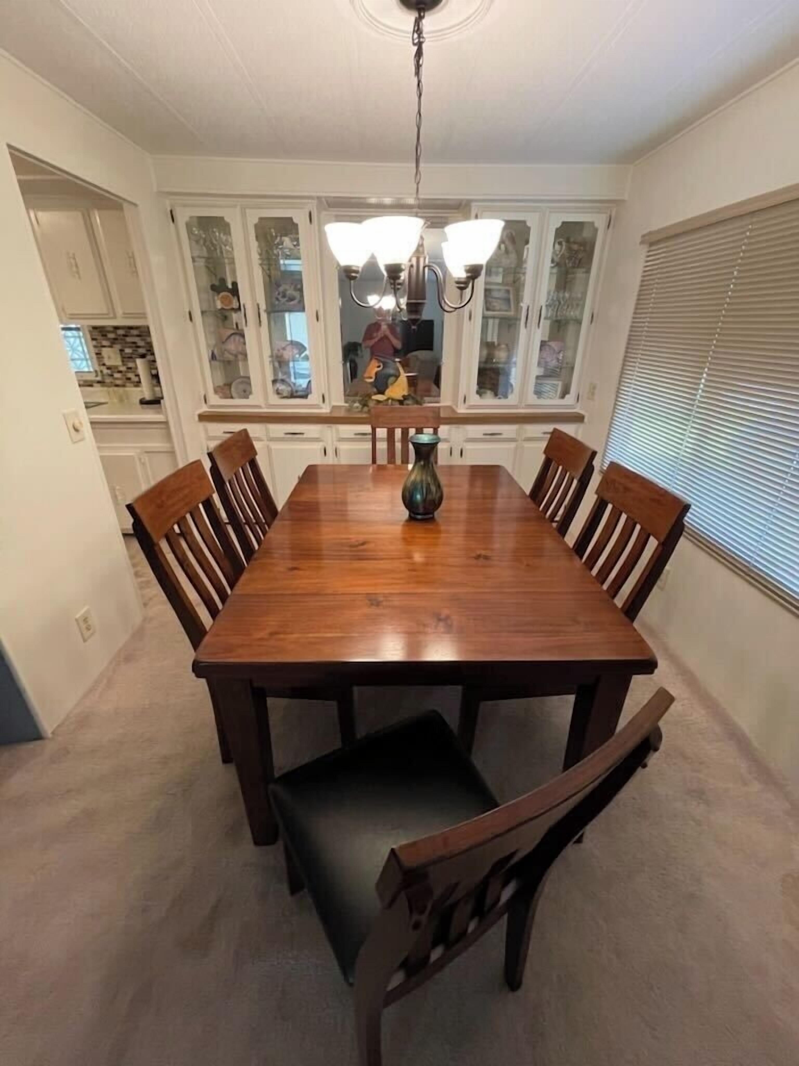 Une salle à manger avec une table en bois, des chaises, un lustre et une fenêtre avec des stores.