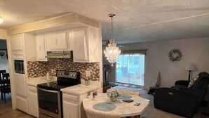 A modern kitchen with white cabinets, a black stove, and a dining area with a round table and chairs. - Lakefront Retreat • Patio + Grill • Pet Friendly (Leesburg)
