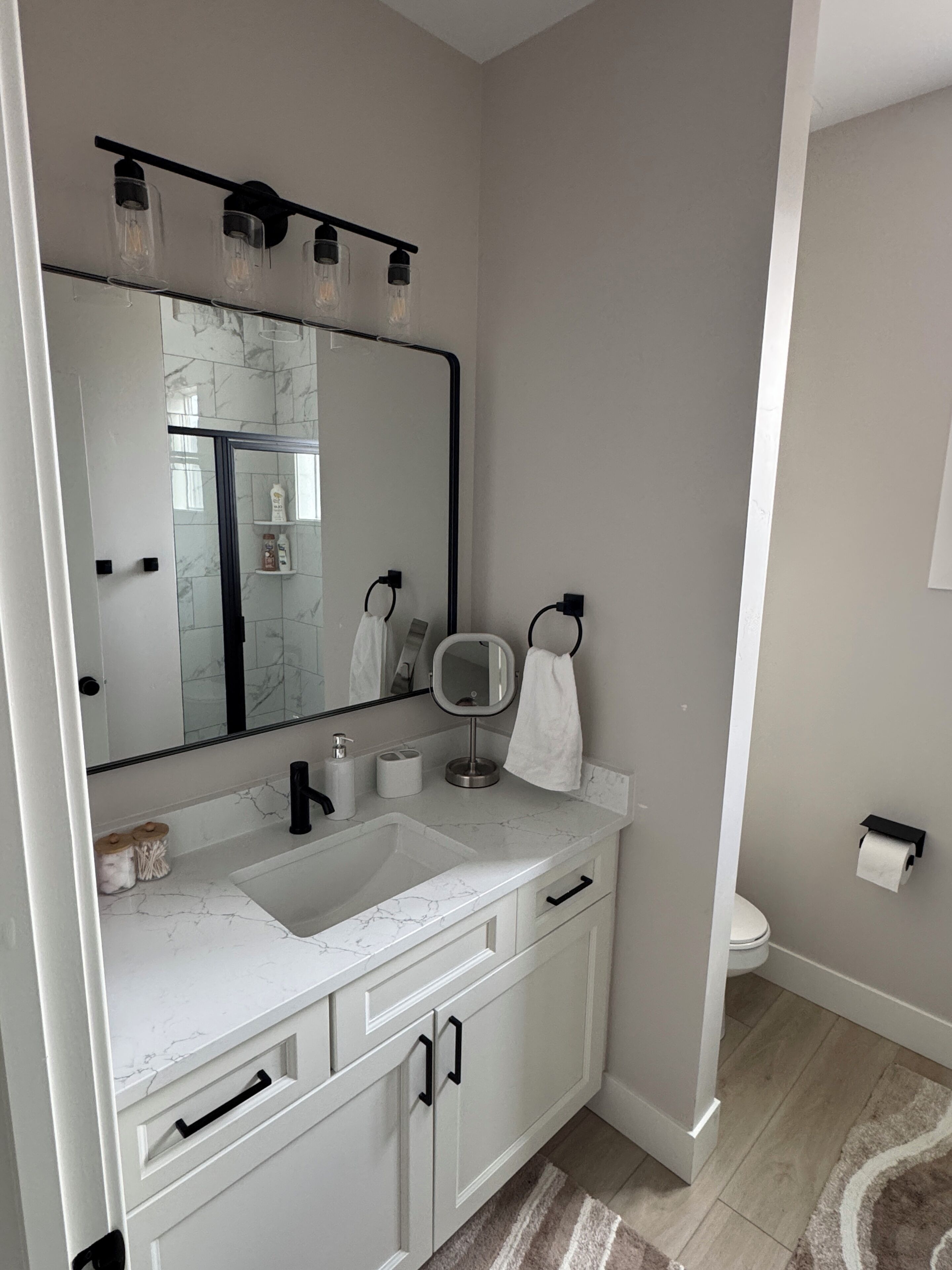Une salle de bain moderne avec un grand miroir, deux lavabos, des toilettes et un espace douche.