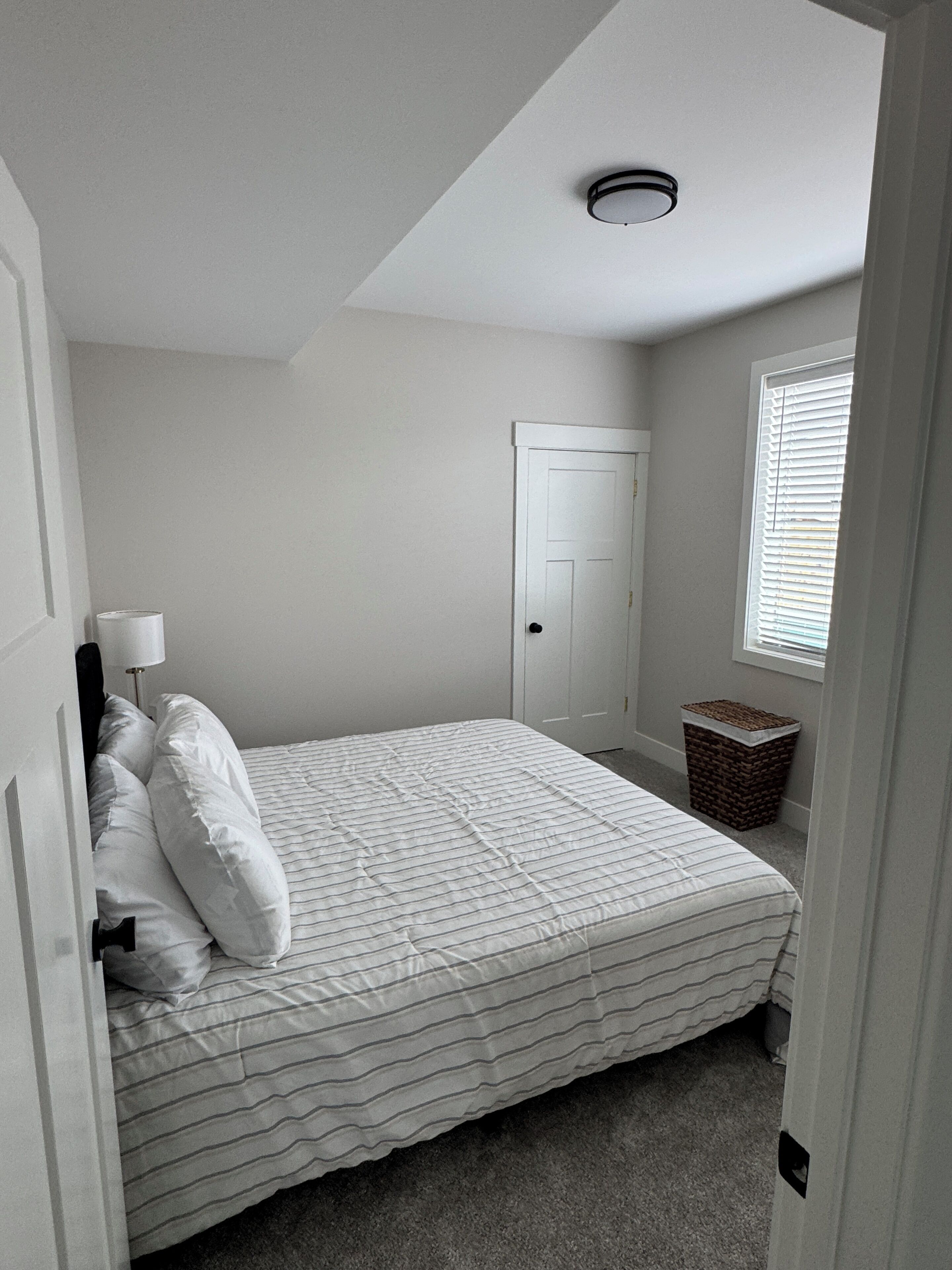 A bedroom with a bed, a door, a window, and a ceiling light.