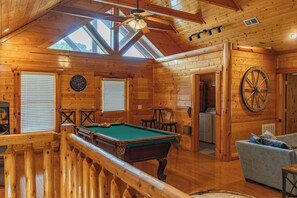 Interior em madeira com mesa de bilhar, um relógio e uma grande roda.