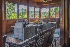A covered outdoor seating area with wicker furniture, large windows, and a view of the outdoors. - 5BR/5BA Cabin | Views, Hot Tub & Pool Table (sevierville)