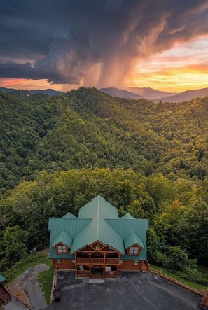 Uma hospedaria com telhado verde, rodeada por uma floresta densa, e um céu tempestuoso acima.