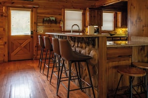 A wooden interior with a bar area, bar stools, a sink, and a window with blinds. - 5BR/5BA Cabin | Views, Hot Tub & Pool Table (sevierville)