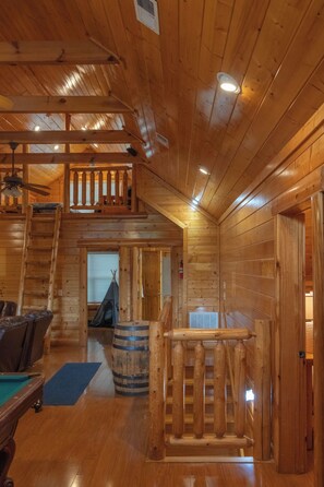 Un interior de madera con una escalera, una mesa de billar y una zona de bar.