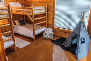 Una habitación tipo cabaña de madera con literas, una tienda de campaña pequeña y una ventana con persianas.