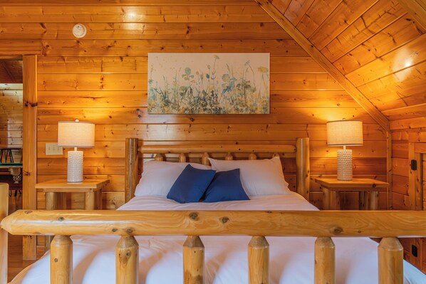 Quarto de cabana de madeira com uma cama, duas luminárias de cabeceira e um quadro na parede.