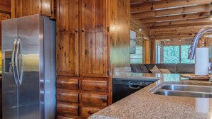 A kitchen with a stainless steel refrigerator, wooden cabinets, a granite countertop, and a dishwasher. - 5BR/5BA Cabin | Views, Hot Tub & Pool Table (sevierville)