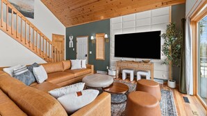 Un salon moderne avec un plafond en bois, un grand téléviseur à écran plat, un canapé en cuir et un escalier.