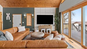 Un salon moderne doté d’un grand téléviseur, d’un plafond en bois et de grandes fenêtres.