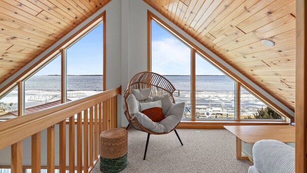 Une pièce avec un plafond en pente, de grandes fenêtres, un fauteuil en osier, une petite table et une vue sur la plage.