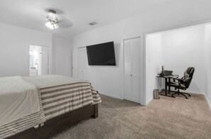 Ein Schlafzimmer mit einem Bett, einem Schreibtisch mit Stuhl, einem Fernseher und einem Deckenventilator.
