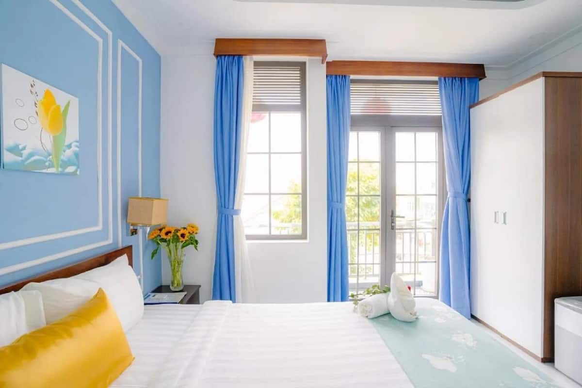 A hotel room with a bed, a nightstand, a lamp, a vase with flowers, and a window with curtains.