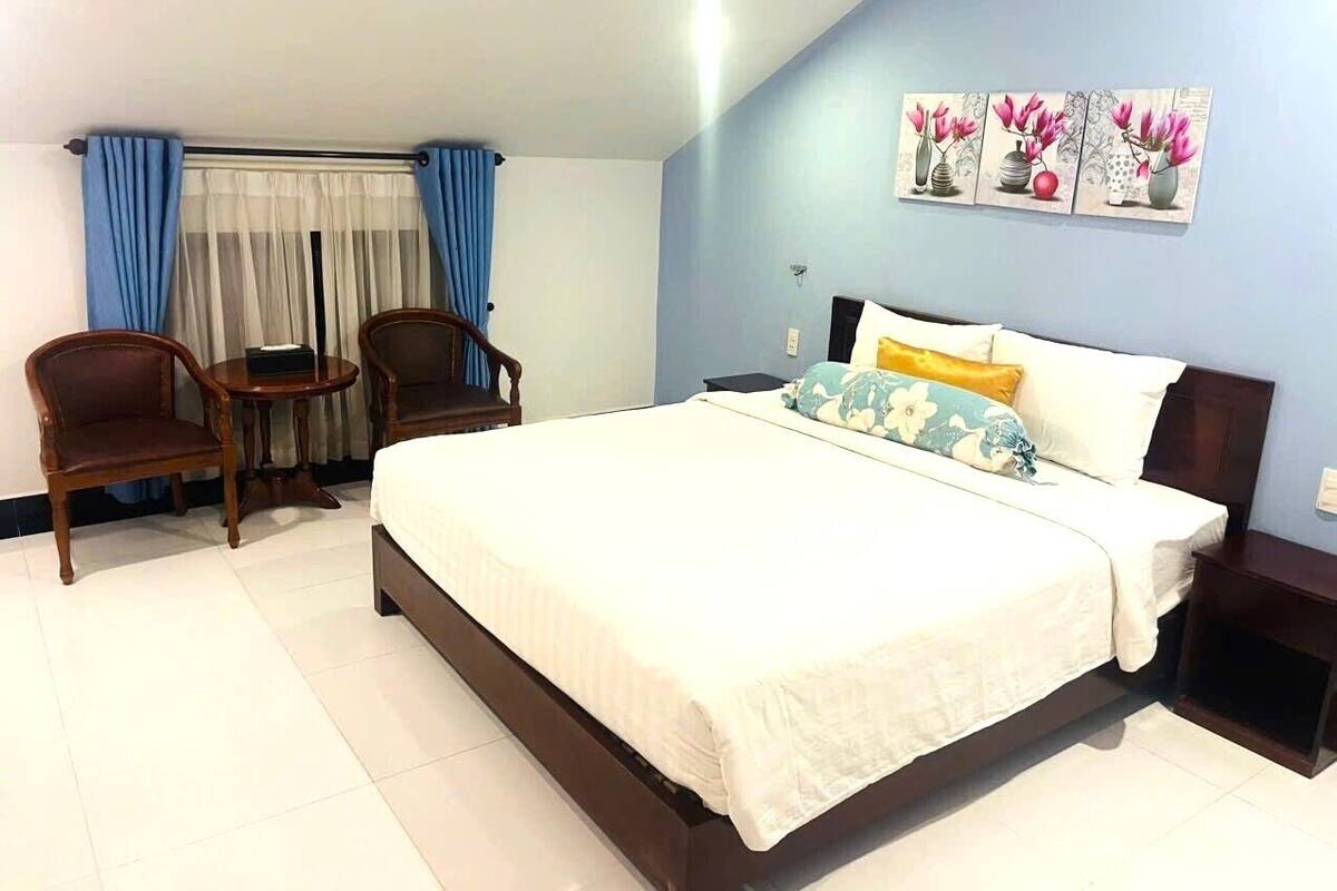 A hotel room with a bed, two chairs, a small table, and a wall-mounted artwork.