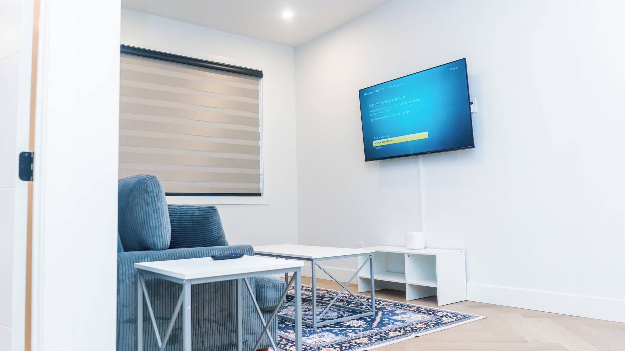Una sala de estar moderna con un televisor de pantalla plana montado en la pared, un sofá azul, una mesita blanca y una alfombra estampada.