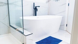 Une salle de bain moderne avec une baignoire sur pieds, une douche à parois de verre et un tapis de bain bleu.