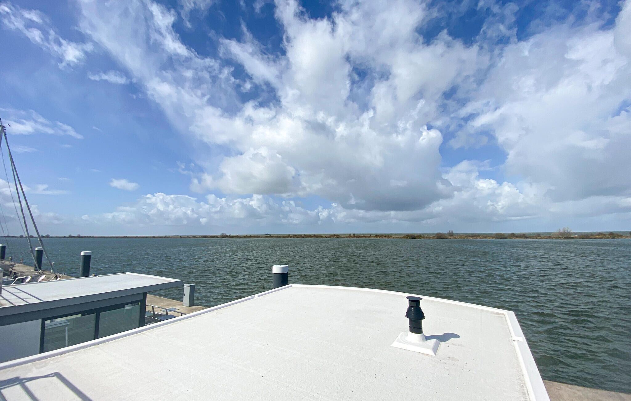 Een scheepsdek met een reling, een waterlichaam op de achtergrond en een gedeeltelijk bewolkte lucht.