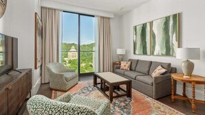 Ein modernes Wohnzimmer mit Sofa, Sessel, Couchtisch und Blick auf ein Gebäude durch große Fenster.