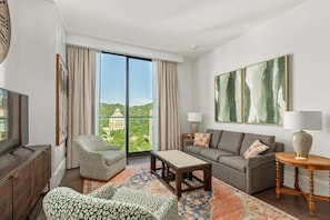 A modern living room with a sofa, armchair, coffee table, and a view of a building through large windows. - The Views Over Pack Square | Arras Vacation Rental (Asheville)