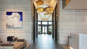 Eine moderne Hotelhalle mit einer langen Rezeption, einer Sitzecke mit Sofa und Sesseln, einem großen Kunstwerk mit einer Wolke und einer dekorativen Decke.